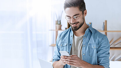 Junger Mann mit Brille schaut auf sein Smartphone.