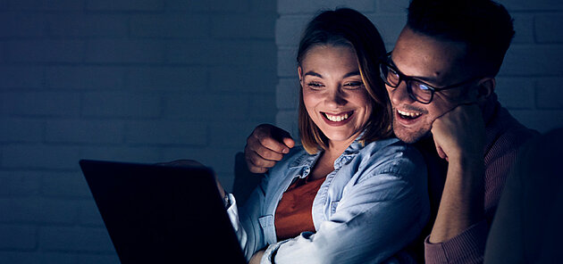 Pärchen sitzt im Dunkeln vor einem Laptop und schauen IPTV.