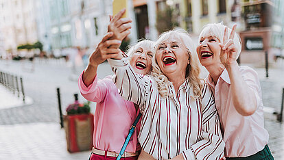 Drei moderne, ältere Damen machen ein Selfie auf der Straße.